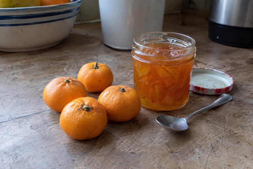 De petits agrumes orange près d’un pot de confiture sur un plan de travail.