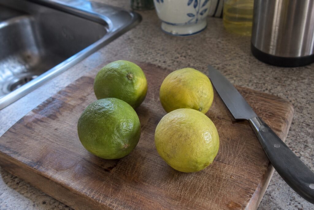 Des agrumes arrondis verts et jaunes posés près d’un couteau sur une planche de cuisine.