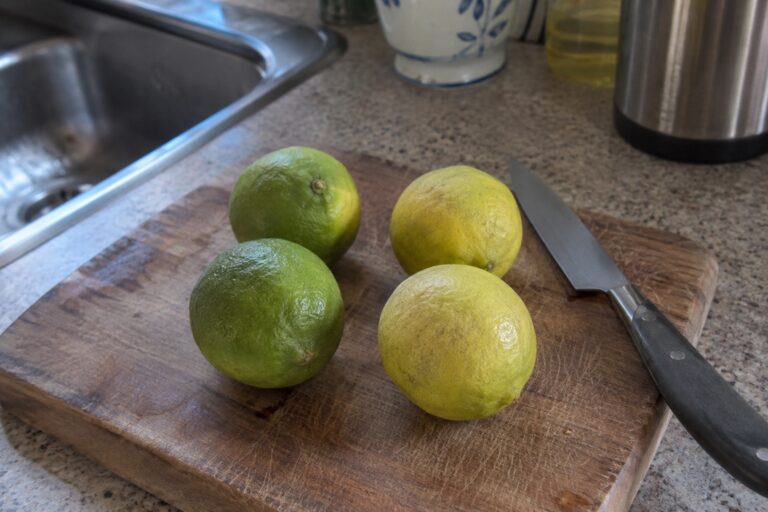 Des agrumes arrondis verts et jaunes posés près d’un couteau sur une planche de cuisine.