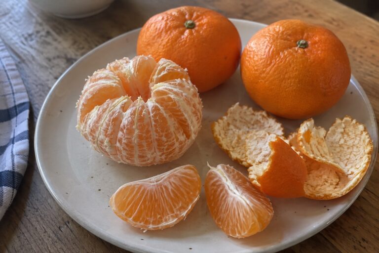 Une mandarine pelée avec ses quartiers et deux fruits entiers sur une assiette.