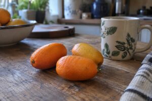 Trois kumquats allongés orange de grand calibre posés sur une table de cuisine.