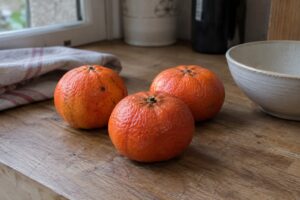 Trois mandarines Satsuma Dobashi Beni aux écorces rouge orangé sur un plan de cuisine.