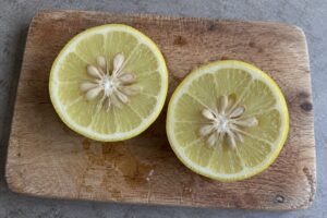 Agrume jaune coupé en deux montrant sa pulpe claire et ses nombreux pépins sur une planche de cuisine.