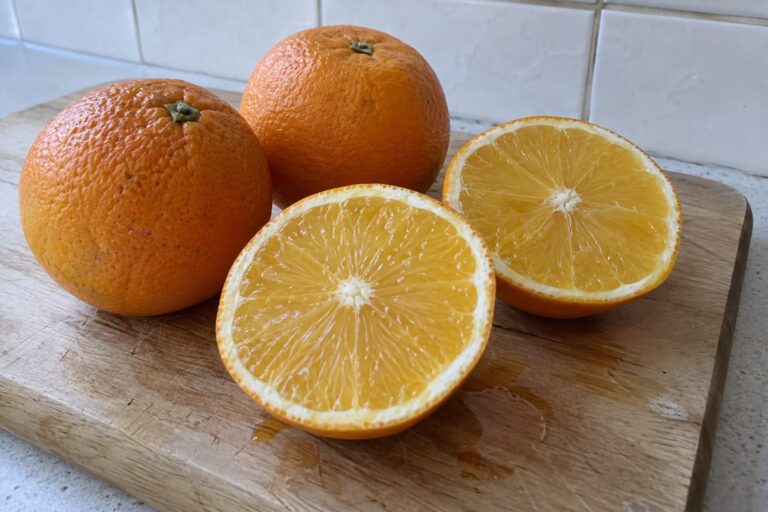 Oranges entières et orange coupée en deux montrant une pulpe jaune orangé dans une cuisine.
