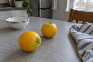 Deux agrumes jaunes posés près d’un bol et d’un torchon sur une table de cuisine.